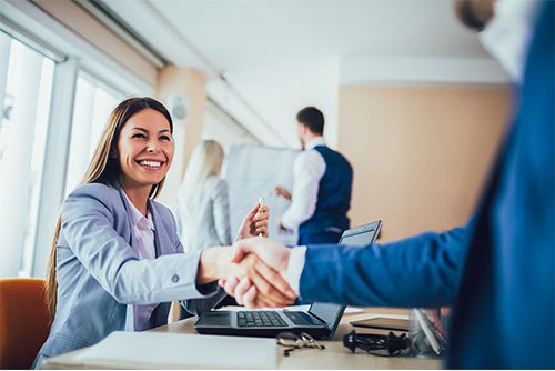 About Us - 2019 Professionally Dressed Woman Shaking Hands with Man at Desk in the Office