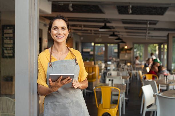 small business owner standing at doorway of her business holding a tablet ready for customers